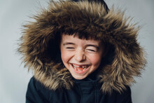 Close-up Of Happy Boy In Fur Coat Standing Against White Background