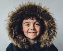Portrait Of Boy In Fur Coat Standing Against White Background