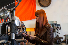 Female Biker Examining Motorcycle In Garage