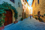 Fototapeta Uliczki - Cozy street decorated with colorful flowers, Pienza, Tuscany, Italy, Europe. Narrow street in the charming town of Pienza in Tuscany. Beautiful streets of the small and historic village Pienza, Italy