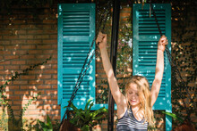 Cute Girl With Blond Hair Swinging Against Brick Wall In Yard