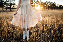 Low Section Of Girl Holding Her Dress While Standing Amidst Plants On Field During Sunset