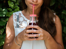 Midsection Of Woman Drinking Fruit Juice While Standing Against Plants In Park