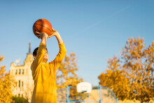 Low Angle View Of Boy Throwing Basketball While Standing Against Clear Blue Sky During Sunny Day