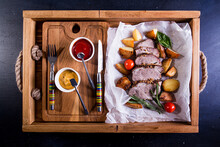 Overhead View Of Cooked Pork With Potatoes And Tomatoes In Wooden Tray On Table