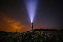 Side View Of Man Holding Illuminated Flashlight While Standing On Hill Against Star Field At Night
