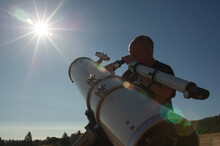 Low Angle View Of Astronomer Looking Bright Sun Through Telescope Against Clear Sky During Sunny Day