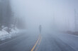© Cavan Images - Rear view of woman walking on road in Yellowstone National park during foggy weather
