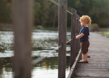Young Boy Looks Out At Pond From Dock