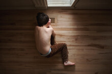Young Boy With No Shirt Looking Into Heating Vent On The Floor