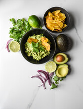 Bowl Of Guacamole And Chips With It's Ingredients On A Marble Counter.