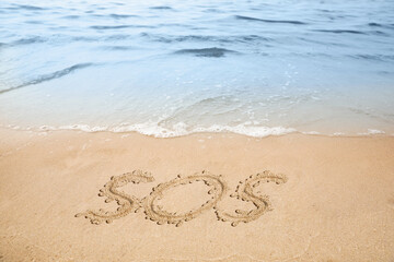 SOS message drawn on sandy beach near sea