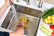 A hand shoves food waste into a disposer hole in the kitchen sink