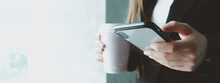 Young Woman In Focus Looking Phone, Holding A Cup With Coffee At Office.-panoramic Banner