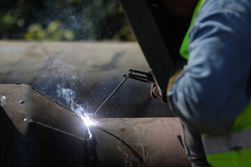 Shallow depth of field (selective focus) details with a professional welder welding an industrial metallic pipeline.