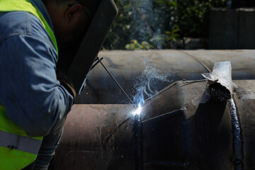 Shallow depth of field (selective focus) details with a professional welder welding an industrial metallic pipeline.