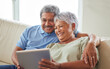 © Alex S/peopleimages.com - Senior couple, tablet and communication on social media or video call with elderly husband and wife relaxing on the couch at home. Man and woman reading retirement savings insurance on a banking app