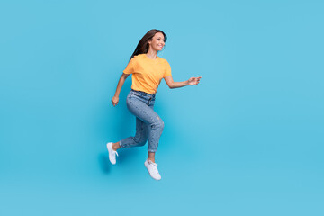 Wall Mural - Full length photo of shiny sweet girl dressed yellow t-shirt jumping high running fast empty space isolated blue color background