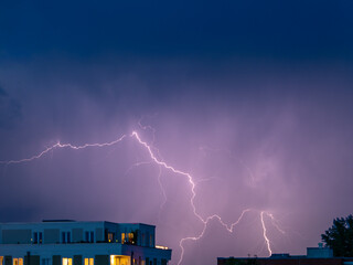 Lightning sparkles over the houses of the city during a thunderstorm. Thunderstorm with lightning.