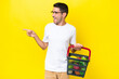 Young handsome man holding a shopping basket full of food over isolated yellow background pointing finger to the side and presenting a product