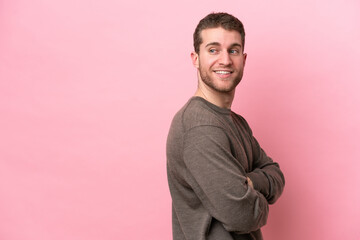 Wall Mural - Young caucasian man isolated on pink background with arms crossed and happy