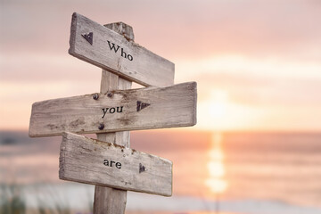who you are text quote engraved on wooden signpost outdoors on the beach with sunset theme.