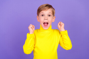 Photo of overjoyed positive boy raise fists achievement shout yes hooray luck isolated on violet color background