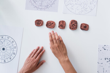 top view of cropped oracle near clay runes and star charts on table.