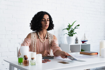Wall Mural - young woman predicting on tarot cards near blurred candles and essential oils.