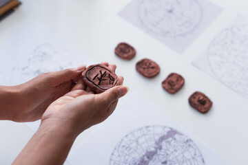 Wall Mural - high angle view of cropped fortune teller holding clay rune near blurred star charts.