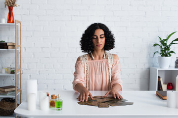 Wall Mural - brunette fortune teller predicting on tarot cards near candles and bottles with essential oils.