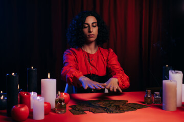 Wall Mural - KYIV, UKRAINE - JUNE 29, 2022: fortune teller divinating on tarot cards near burning candles on red table in darkness.