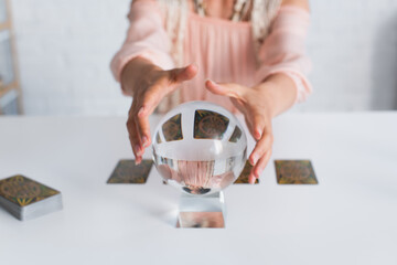Wall Mural - KYIV, UKRAINE - JUNE 29, 2022: selective focus of crystal ball near cropped fortune teller on blurred background.