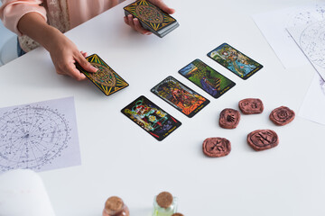 Wall Mural - KYIV, UKRAINE - JUNE 29, 2022: high angle view of cropped fortune teller predicting on tarot cards near clay runes.
