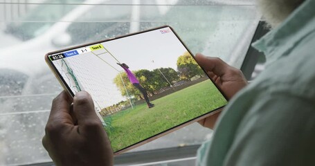 Poster - Video of african american man sitting on sofa and watching football on tablet at home