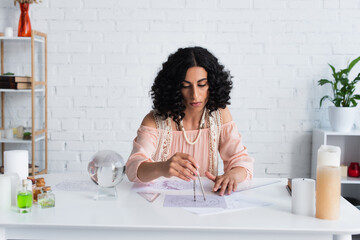 Wall Mural - young astrologist drawing star charts near crystal ball and candles at home.