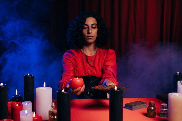 Wall Mural - brunette fortune teller with candle and tarot cards near blue smoke on dark background.