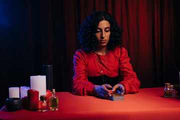 Wall Mural - brunette medium sitting near tarot cards and candles on dark background with red drape.