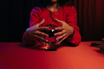 Wall Mural - cropped view of medium holding hands near crystal ball during spiritual session on dark background.