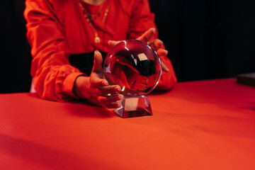 Wall Mural - partial view of fortune teller near crystal ball on red table isolated on black.