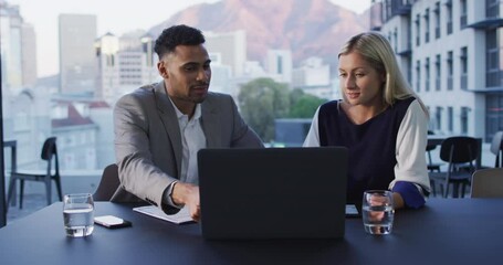 Wall Mural - Video of two diverse male and female colleagues discussing and using laptop in office