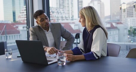 Wall Mural - Video of two diverse male and female colleagues discussing and using laptop in office