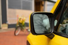 Selective Focus Shot Of A Rearview Side Mirror Of A Yellow Car Covered With Rain.