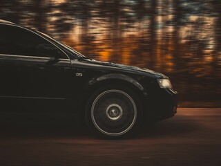 Closeup of a black car driving on the road against the blurry background.