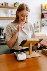 Blonde white barista woman working with tablet computer in cafe