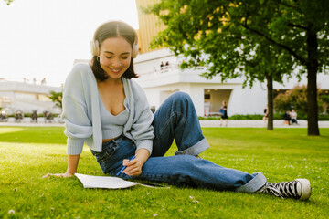 Young beautiful smiling asian girl in headphones holding pen