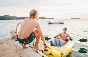 Wall Mural - Father with teenager son on the bright yellow inflatable kayak returning back from evening ride by the Adriatic sea harbor in Croatia near from Sibenik city. Vacation and family values vertical image.