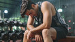 Close-up or closeup shot of Asian male bodybuilder in sportswear is sitting on fitness bench and feeling tired after weight training workout. Athlete man with exhaustion is resting on fitness bench.