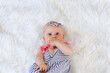 Cute baby girl in striped dress and pale blue headband lying on on a white fur blanket.