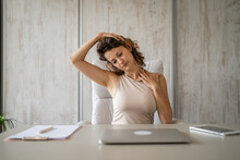 Young Woman Stretching At Work While Sitting At Desk Having Neck Pain